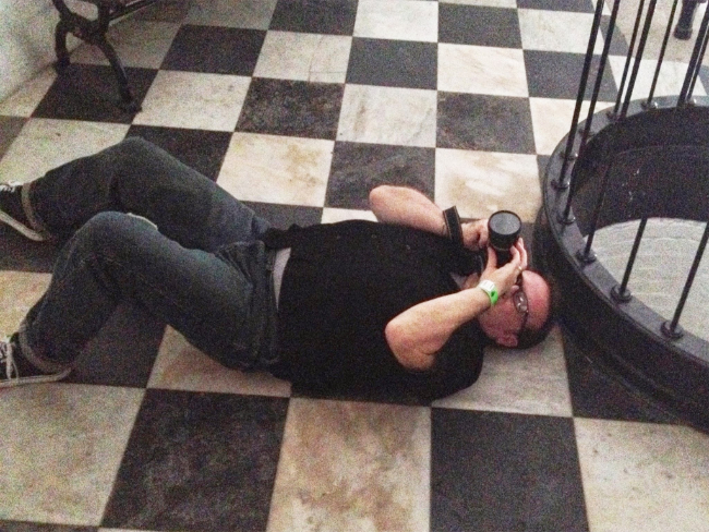 Steven Mikel lying on his back at the base of the lighthouse stairway taking the photograph he used as a reference for the
                painting entitled Wickie Way